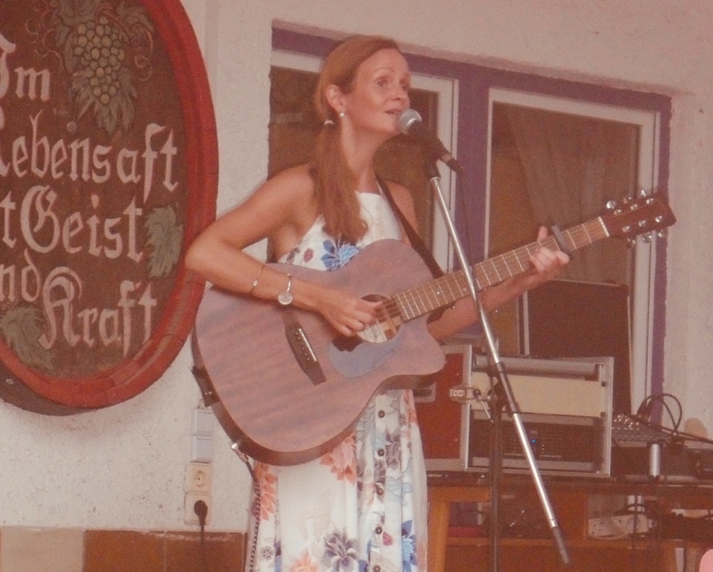 Kira Ludlow mit Gitarre und Mikrofon bei einem Auftritt